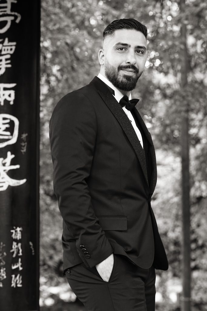 Schwarzwei&szlig; Hochzeitsfotografie und Potrait des Br&auml;utigam in schickem Smoking im Rahmen ihrer Hochzeit. Die Sonne scheint ihr ins Gesicht w&auml;hrend sie in der Natur des Asiatischen Garten in der N&auml;he von Frankfurt am Main steht