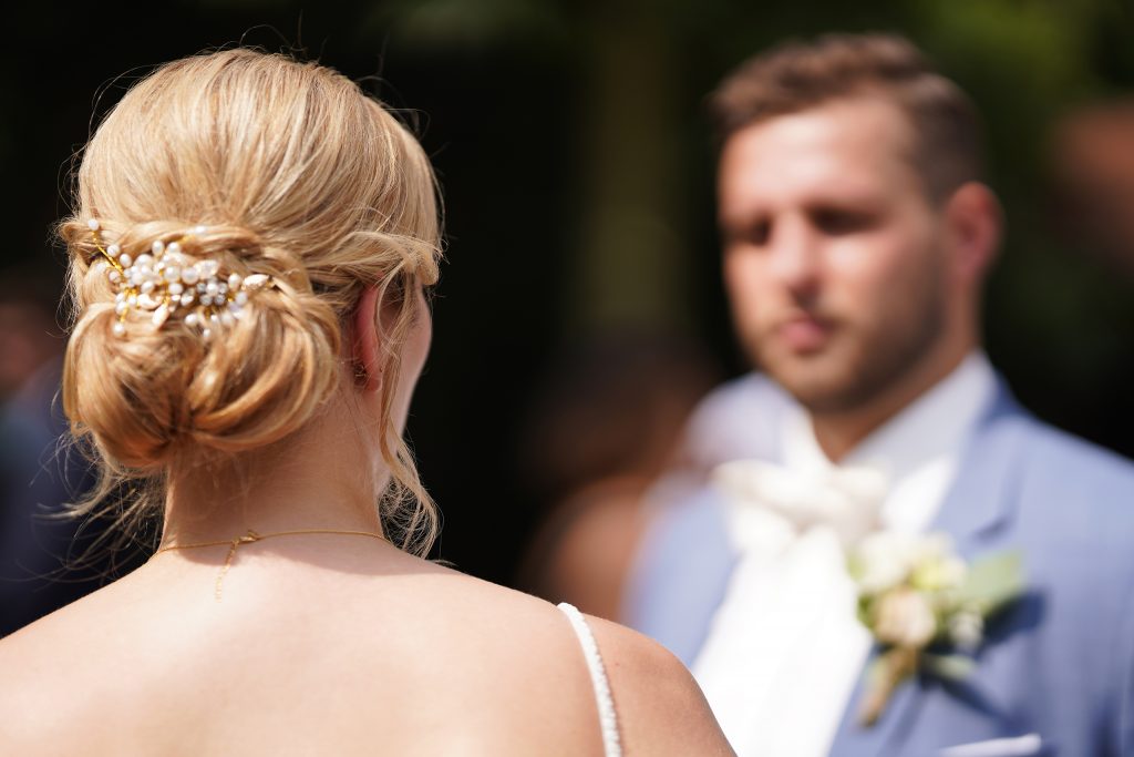 Hochzeitsfotografie einer jungen attraktiven Frau im Rahmen einer Hochzeit als Braut. Die Sonne scheint ihr ins Gesicht w&auml;hrend sie aus der Kirche von Hanau in der N&auml;he von Frankfurt am Main kommt. Sie tr&auml;gt ein schickes Brautkleid