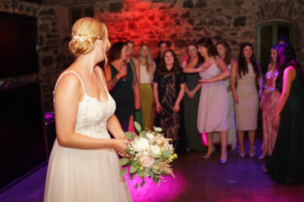 Hochzeitsfotografie von Wurf des Brautstrau&szlig; auf der Hochzeitsfeier und Party eines Brautpaars in schickem Brautkleid und Anzug im Rahmen einer Hochzeit. Sie feiern in einer sch&ouml;nen Location in Hanau in der N&auml;he von Frankfurt am Main. Sie genie&szlig;en ihren besonderen Tag. Die Trauzeuginnen und G&auml;ste stehen hinter der Braut. Alle tragen sch&ouml;ne Kleider und freuen sich auf den Moment