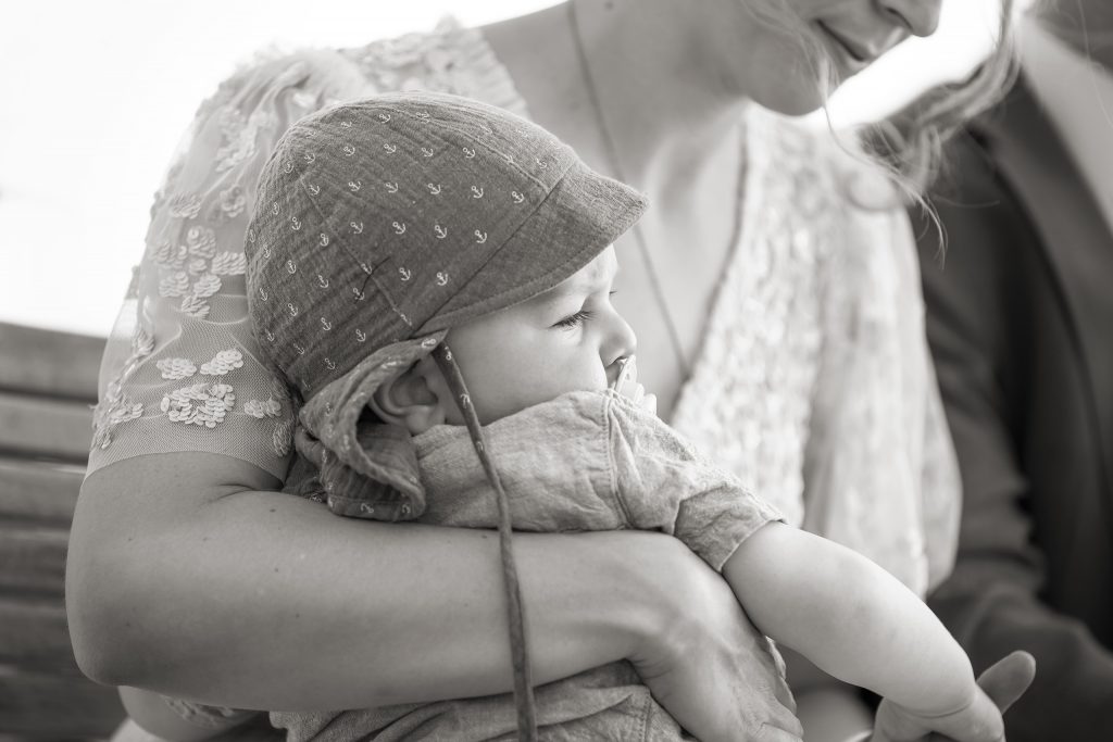 Hochzeitsfotografie von der standesamtlichen Trauung eines Brautpaars in schickem Brautkleid und Anzug im Rahmen einer Hochzeit. Die Sonne scheint in der Natur auf der Burg von Kronberg im Taunus in der N&auml;he von Frankfurt am Main. Sie tr&auml;gt ihren Brautstrau&szlig; in der Hand. Neben ihnen sitzen ihre Trauzeugen. Die Standesbeamte sitzt vor ihnen. Sie haben einen sch&ouml;nen Ausblick auf die Altstadt und den Taunus. Hinter ihnen sitzen ihre Familien.