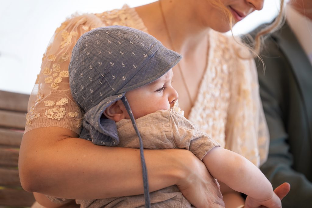 Hochzeitsfotografie von der standesamtlichen Trauung eines Brautpaars in schickem Brautkleid und Anzug im Rahmen einer Hochzeit. Die Sonne scheint in der Natur auf der Burg von Kronberg im Taunus in der N&auml;he von Frankfurt am Main. Sie tr&auml;gt ihren Brautstrau&szlig; in der Hand. Neben ihnen sitzen ihre Trauzeugen. Die Standesbeamte sitzt vor ihnen. Sie haben einen sch&ouml;nen Ausblick auf die Altstadt und den Taunus. Hinter ihnen sitzen ihre Familien.