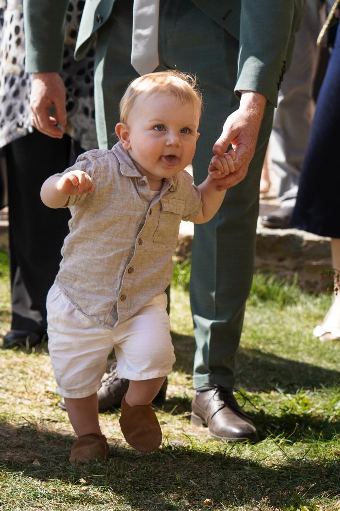 Hochzeitsfotografie von der standesamtlichen Trauung eines Brautpaars in schickem Brautkleid und Anzug im Rahmen einer Hochzeit. Die Sonne scheint in der Natur auf der Burg von Kronberg im Taunus in der N&auml;he von Frankfurt am Main. Sie steckt ihrem Mann den Ehering an die Hand und der steckt ihr den Ring an ihre Hand. Neben ihnen sitzen ihre Trauzeugen. Die Standesbeamte sitzt vor ihnen. Sie haben einen sch&ouml;nen Ausblick auf die Altstadt und den Taunus. Hinter ihnen sitzen ihre Familien.