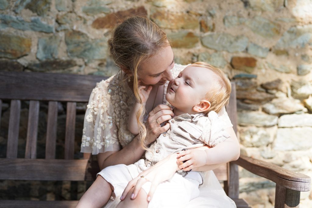 Hochzeitsfotografie von der standesamtlichen Trauung eines Brautpaars in schickem Brautkleid und Anzug im Rahmen einer Hochzeit. Die Sonne scheint in der Natur auf der Burg von Kronberg im Taunus in der N&auml;he von Frankfurt am Main. Sie steckt ihrem Mann den Ehering an die Hand und der steckt ihr den Ring an ihre Hand. Neben ihnen sitzen ihre Trauzeugen. Die Standesbeamte sitzt vor ihnen. Sie haben einen sch&ouml;nen Ausblick auf die Altstadt und den Taunus. Hinter ihnen sitzen ihre Familien. Sie haben viel Spa&szlig; auf ihrer Hochzeitsfeier und Party.