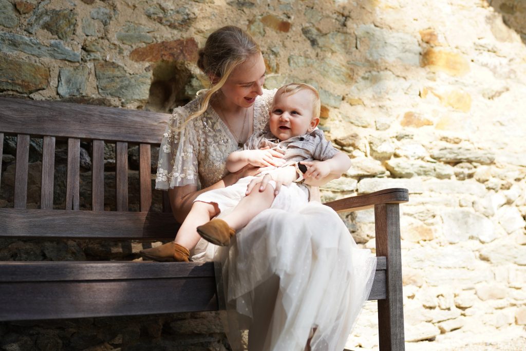 Hochzeitsfotografie von der standesamtlichen Trauung eines Brautpaars in schickem Brautkleid und Anzug im Rahmen einer Hochzeit. Die Sonne scheint in der Natur auf der Burg von Kronberg im Taunus in der N&auml;he von Frankfurt am Main. Sie steckt ihrem Mann den Ehering an die Hand und der steckt ihr den Ring an ihre Hand. Neben ihnen sitzen ihre Trauzeugen. Die Standesbeamte sitzt vor ihnen. Sie haben einen sch&ouml;nen Ausblick auf die Altstadt und den Taunus. Hinter ihnen sitzen ihre Familien. Sie haben viel Spa&szlig; auf ihrer Hochzeitsfeier und Party.