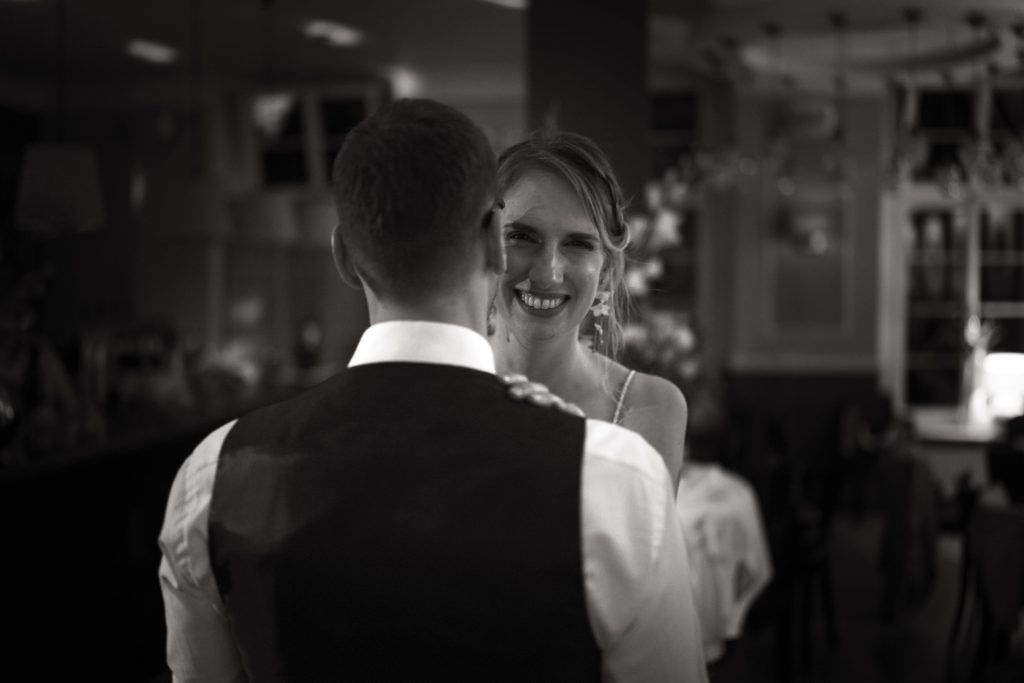 Schwarzwei&szlig; Hochzeitsfotografie vom Hochzeitstanz eines Brautpaars in schickem Brautkleid und Anzug im Rahmen einer Hochzeit. Sie tanzen in Aschaffenburg in der N&auml;he von Frankfurt am Main stehen. Die Braut lacht in die Kamera