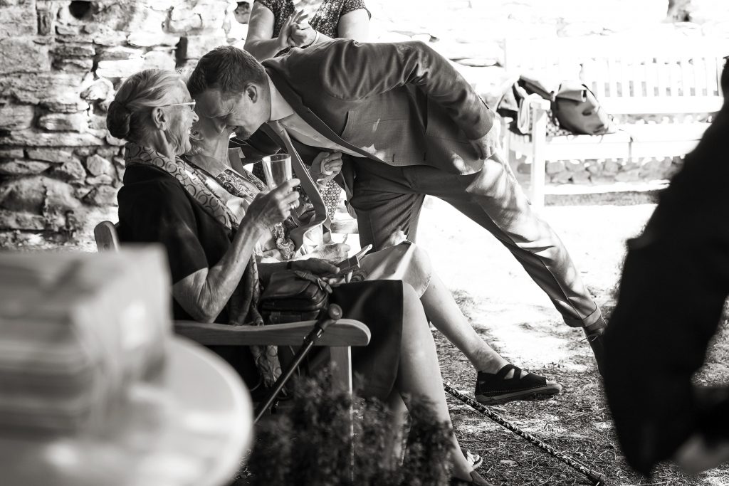 Schwarzwei&szlig; Hochzeitsfotografie von der standesamtlichen Trauung eines Brautpaars in schickem Brautkleid und Anzug im Rahmen einer Hochzeit. Die Sonne scheint in der Natur auf der Burg von Kronberg im Taunus in der N&auml;he von Frankfurt am Main. Sie steckt ihrem Mann den Ehering an die Hand und der steckt ihr den Ring an ihre Hand. Neben ihnen sitzen ihre Trauzeugen. Die Standesbeamte sitzt vor ihnen. Sie haben einen sch&ouml;nen Ausblick auf die Altstadt und den Taunus. Hinter ihnen sitzen ihre Familien. Sie haben viel Spa&szlig; auf ihrer Hochzeitsfeier und Party.