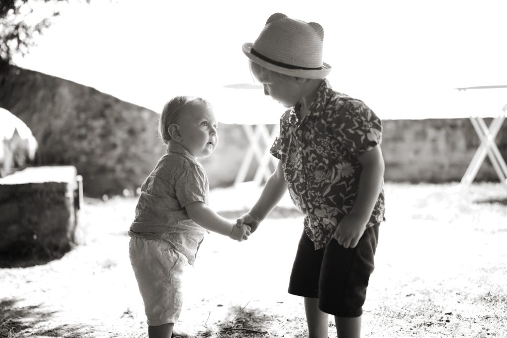 Schwarzwei&szlig; Hochzeitsfotografie von der standesamtlichen Trauung eines Brautpaars in schickem Brautkleid und Anzug im Rahmen einer Hochzeit. Die Sonne scheint in der Natur auf der Burg von Kronberg im Taunus in der N&auml;he von Frankfurt am Main. Sie steckt ihrem Mann den Ehering an die Hand und der steckt ihr den Ring an ihre Hand. Neben ihnen sitzen ihre Trauzeugen. Die Standesbeamte sitzt vor ihnen. Sie haben einen sch&ouml;nen Ausblick auf die Altstadt und den Taunus. Hinter ihnen sitzen ihre Familien. Sie haben viel Spa&szlig; auf ihrer Hochzeitsfeier und Party.