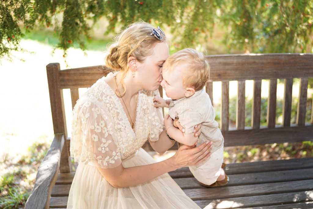 Hochzeitsfotografie von der standesamtlichen Trauung eines Brautpaars in schickem Brautkleid und Anzug im Rahmen einer Hochzeit. Die Sonne scheint in der Natur auf der Burg von Kronberg im Taunus in der N&auml;he von Frankfurt am Main. Sie steckt ihrem Mann den Ehering an die Hand und der steckt ihr den Ring an ihre Hand. Neben ihnen sitzen ihre Trauzeugen. Die Standesbeamte sitzt vor ihnen. Sie haben einen sch&ouml;nen Ausblick auf die Altstadt und den Taunus. Hinter ihnen sitzen ihre Familien. Sie haben viel Spa&szlig; auf ihrer Hochzeitsfeier und Party.