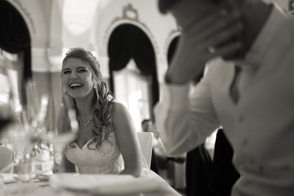 Schwarzwei&szlig; Hochzeitsfotografie von Brautpaar in schickem Brautkleid und Anzug im Rahmen einer Hochzeit in der N&auml;he von Frankfurt am Main. Die Braut lacht herzlich und der Br&auml;utigam kann sein Lachen kaum zur&uuml;ckhalten. Sie genie&szlig;en ihren Hochzeitstag