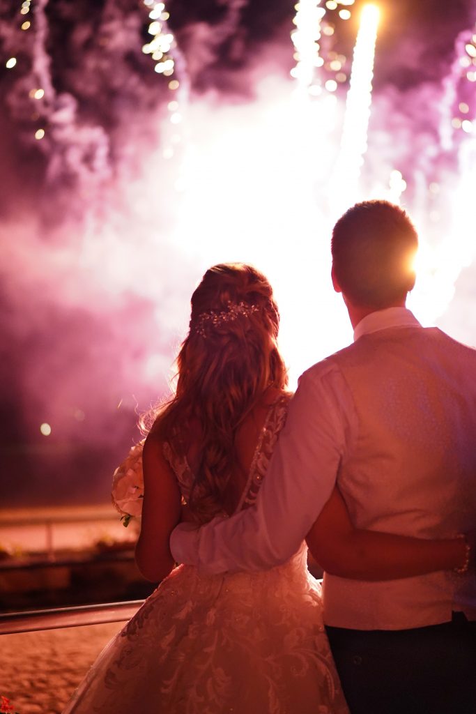Hochzeitsfotografie vom Kuss eines Brautpaars in schickem Brautkleid und Anzug im Rahmen einer Hochzeit. Hinter ihnen leuchtet das Feuerwerk w&auml;hrend sie in der Natur in der N&auml;he von Frankfurt am Main stehen