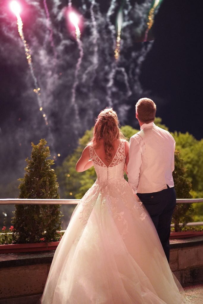 Hochzeitsfotografie vom Kuss eines Brautpaars in schickem Brautkleid und Anzug im Rahmen einer Hochzeit. Hinter ihnen leuchtet das Feuerwerk w&auml;hrend sie in der Natur in der N&auml;he von Frankfurt am Main stehen