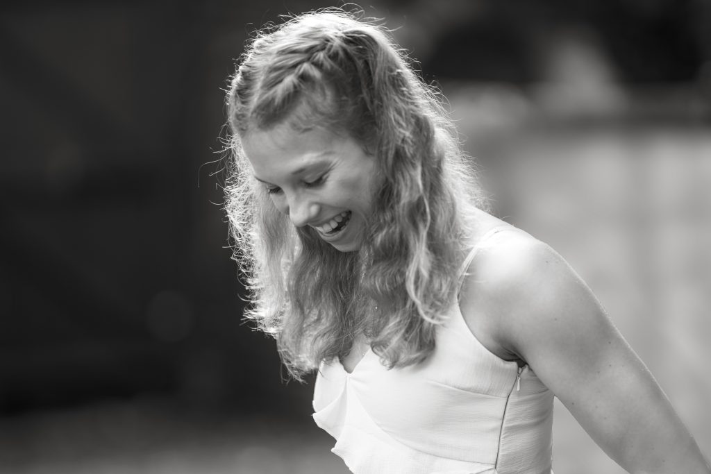 SchwarzWeiß-Fotografie-Hochzeit-Trauzäugin-Sonnenschein-Augen-Licht-Hanau-Frankfurt-Fashion-Mode-Locken SchwarzWeiß-Fotografie einer jungen attraktiven Frau im Rahmen eines Fotoshootings einer Hochzeit als Trauzeugin. Die Sonne scheint in ihre Augen und ihre Locken leuchten. Sie steht in der Natur von Hanau in der Nähe von Frankfurt am Main. Sie trägt ein schickes Kleid