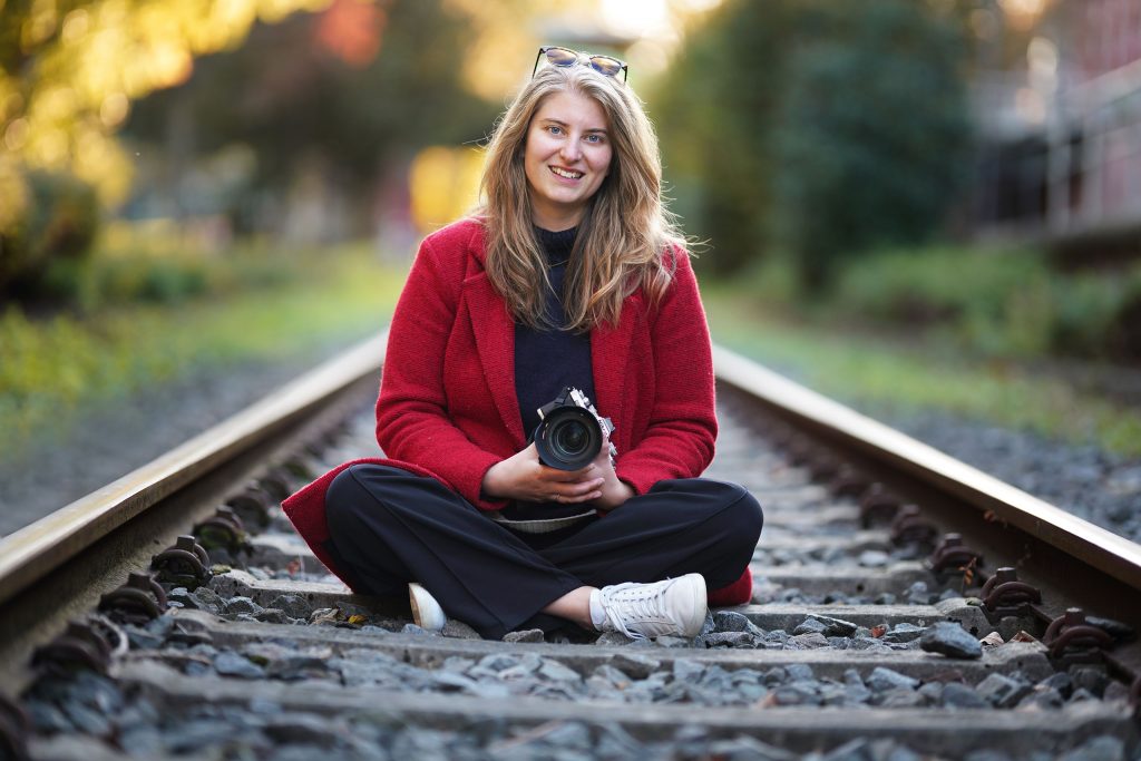 Streetphotography-Fashion-Fotografie-Sonnenschein-Frankfurt-Bahnstrecke-Natur-Fotoshooting-junge Frau Street-Fotografie von junger modischen Frau auf Bahnstrecke in der Nähe von Frankfurter Innenstadt im Sonnenschein mit alter Kamera von Nikon in der Hand