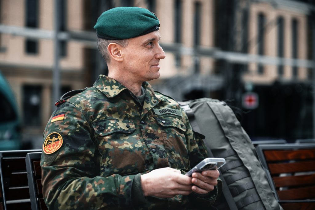 Business-Fotografie von Bundeswehr Soldat und Veteran Marcel Bohnert vom Deutschen Bundeswehrverband am Frankfurter Hauptbahnhof vor dem Start einer Reise im Fleckten-Kampfanzug mit iPhone in der Hand