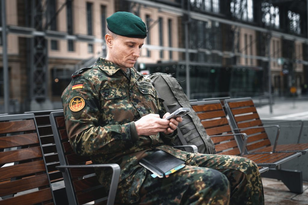 Business-Fotografie von Bundeswehr Soldat und Veteran Marcel Bohnert vom Deutschen Bundeswehrverband am Frankfurter Hauptbahnhof vor dem Start einer Reise im Fleckten-Kampfanzug mit iPhone in der Hand