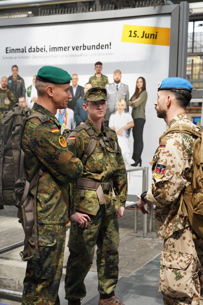 Business-Fotografie von Bundeswehr Soldat und Veteran Marcel Bohnert mit anderen Kameraden und Rekruten am Frankfurter Hauptbahnhof vor dem Start einer Reise im Hintergrund ein Plakat zum Veteranentag in Berlin